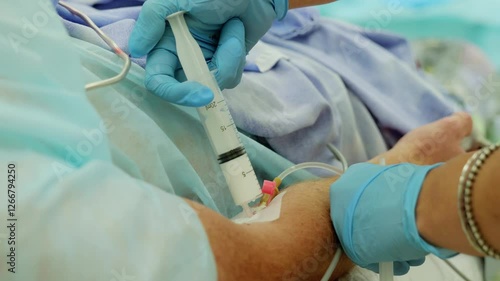 Nurse wearing blue gloves administers medication through an iv catheter in a patient's arm, showcasing a vital healthcare procedure in a hospital environment