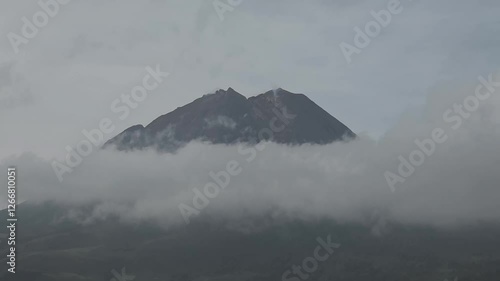 Mount Sinabung partially covered by clouds, creating a dramatic and mysterious volcanic scene. Ideal for nature and documentary projects. photo