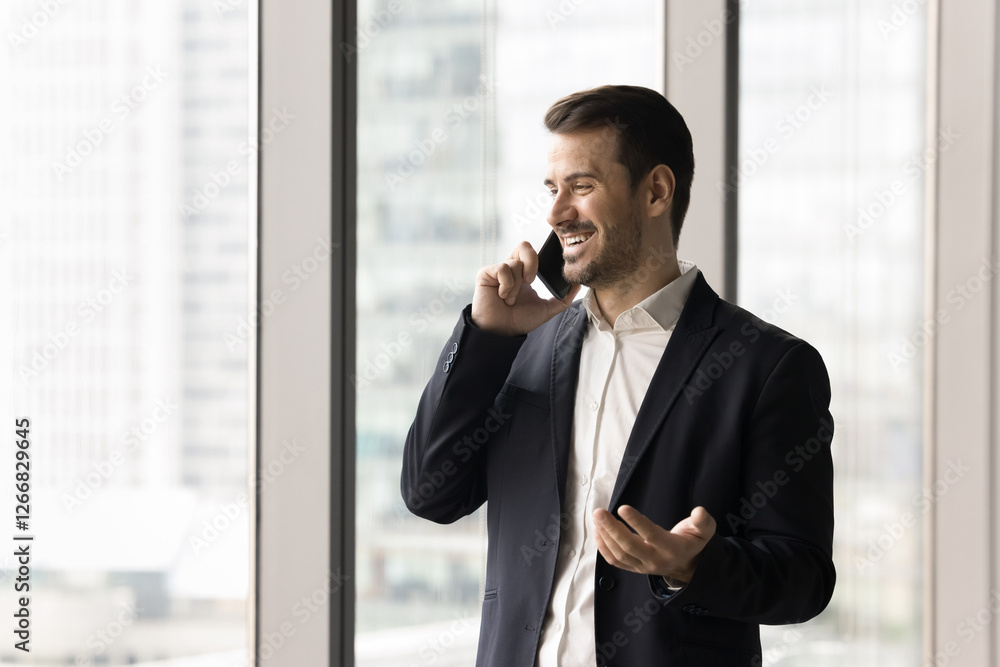 Young businessman, company boss leads formal talk by smartphone, standing near panoramic window with cityscape view. Professional man solve business, consulting, speaks with corporate client remotely Young businessman, company boss leads formal talk by smartphone, standing near panoramic window with cityscape view. Professional man solve business, consulting, speaks with corporate client remotely