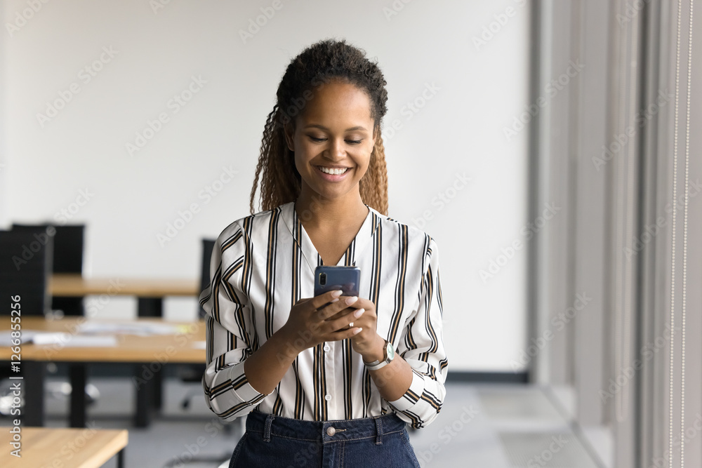African employee using modern smartphone in co-working office, received pleasant message, engage in professional chat with client on her device. Mobile apps usage by personal or business at workplace