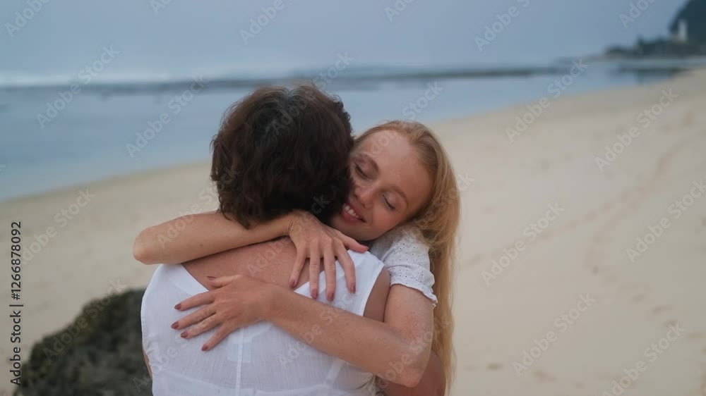 A young redhead woman in white dress, smile and tenderly hugging her senior mother standing on the beach by the ocean. Vacation with family. Adult children traveling with parents. Mothers Day. A young redhead woman in white dress, smile and tenderly hugging her senior mother standing on the beach by the ocean. Vacation with family. Adult children traveling with parents. Mothers Day.