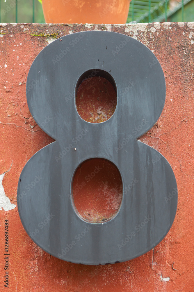 House number 8. Black painted iron over red weathered wall