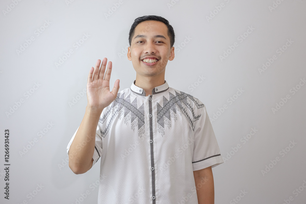 Isolated Muslim Man In White Clothes, Waving His Right Hand With A Friendly Expression, Looking Straight Ahead In A Warm Gesture. Isolated Muslim Man In White Clothes, Waving His Right Hand With A Friendly Expression, Looking Straight Ahead In A Warm Gesture.