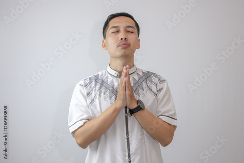 Isolated Muslim Man in White Clothes Praying With Eyes Closed and Hands Together, Isolated in a Moment of Quiet Reflection. photo