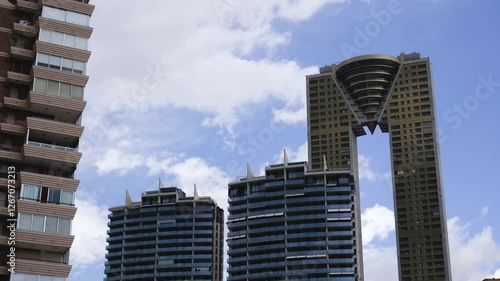 Timelapse of the Intempo Skyscraper in Benidorm, Spain Tallest Building in Costa Blanca golden tower bottom Street View with houses in front of the tower 
and Blue cloudy Sky clouds moving fast 4K HQ