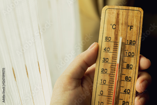 wooden thermometer A man's hand holds a device for measuring high air temperatures inside a residence.
