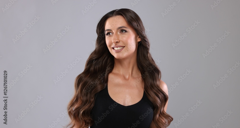 Fototapeta premium Hair styling. Beautiful woman with wavy long hair on grey background