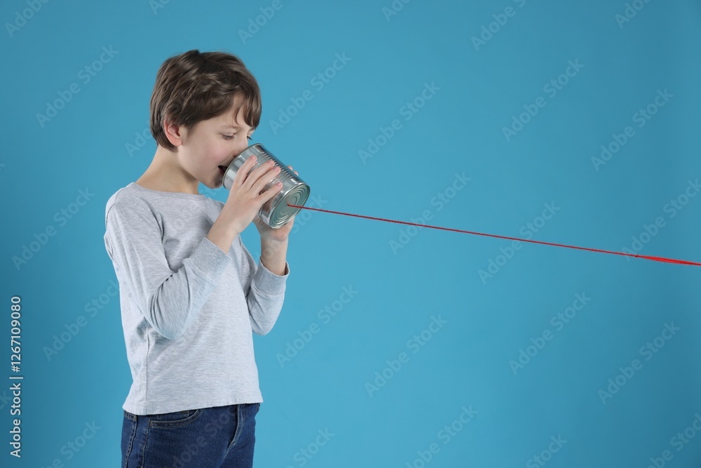 Boy using tin can telephone on blue background Boy using tin can telephone on blue background