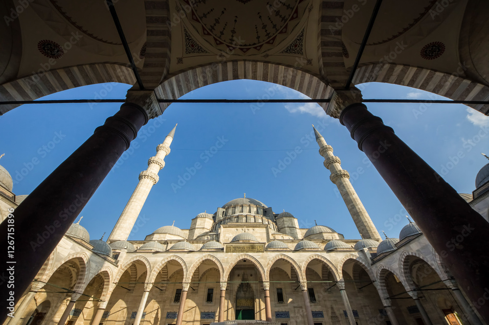 Fototapeta premium Low angle view of Suleymaniye Mosque main dome and minarets framed by courtyard arches against a blue sky, Istanbul, Turkey