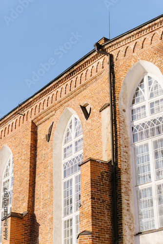 A close-up of a historic red brick building with large arched windows, showcasing intricate architectural details under a bright blue sky. Estonia University of Tartu photo