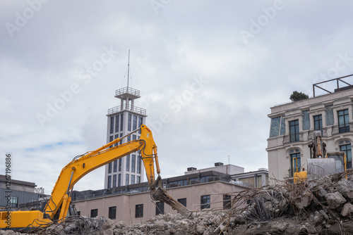 Yellow excavator working on demolition site in urban area. Heavy machinery operating on construction site, tearing down old buildings to make way for new development