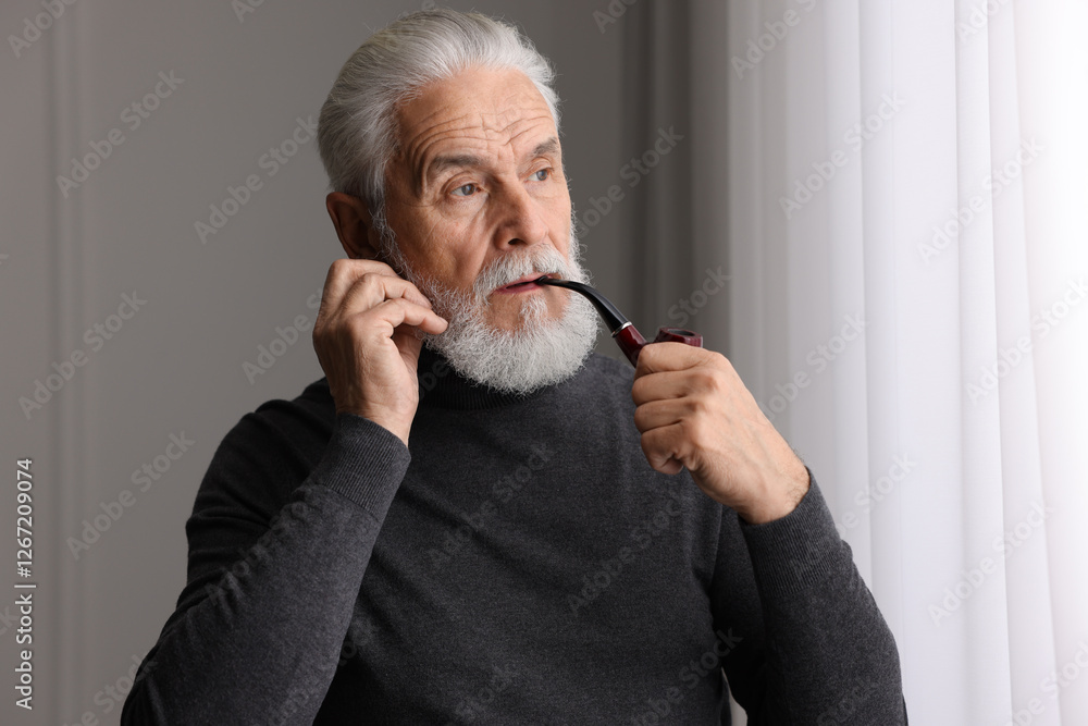 Portrait of handsome bearded man with tobacco pipe near window indoors Portrait of handsome bearded man with tobacco pipe near window indoors