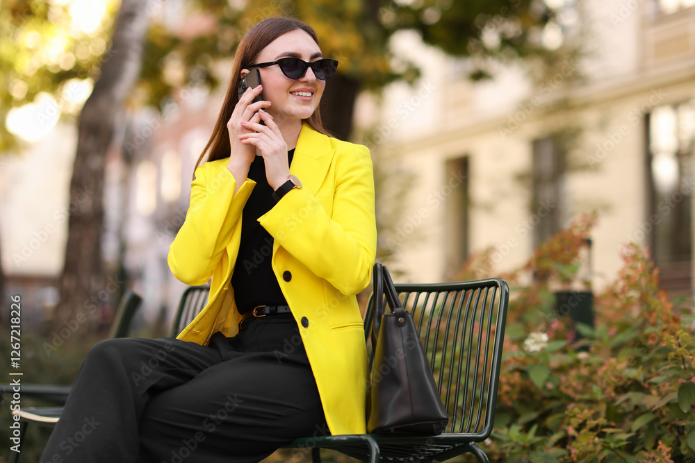 Fototapeta premium Smiling businesswoman in stylish suit talking on smartphone outdoors