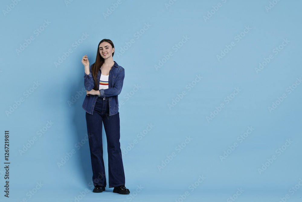 Smiling woman in stylish jeans on light blue background. Space for text Smiling woman in stylish jeans on light blue background. Space for text