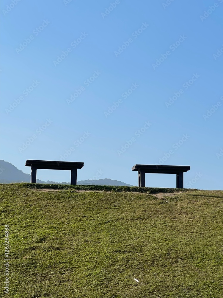 View of two benches are placed on the green grass. Behind is a bright blue sky View of two benches are placed on the green grass. Behind is a bright blue sky