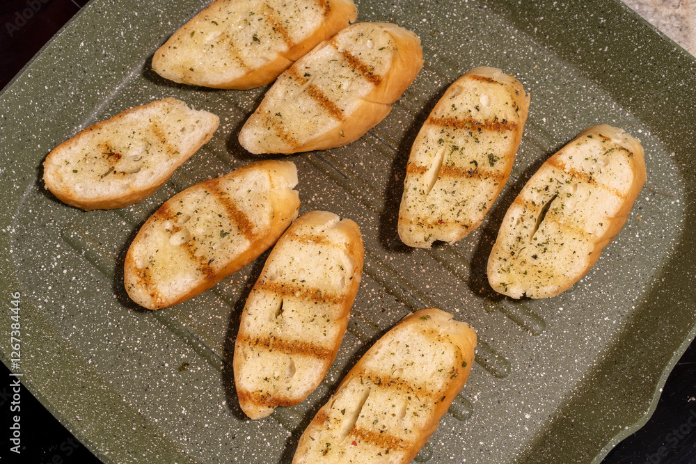 Several slices of seasoned and grilled bread on a speckled non-stick grill pan