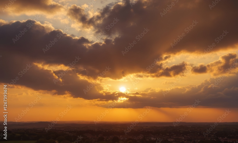 A stunning sunset casting golden hues across the sky, framed by clouds, revealing the serene landscape below.