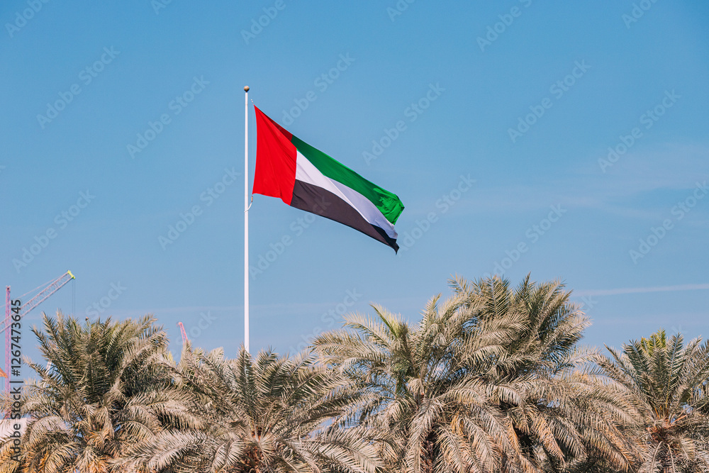 UAE flag waving in the wind on a sunny day with palm trees and blue sky in the background