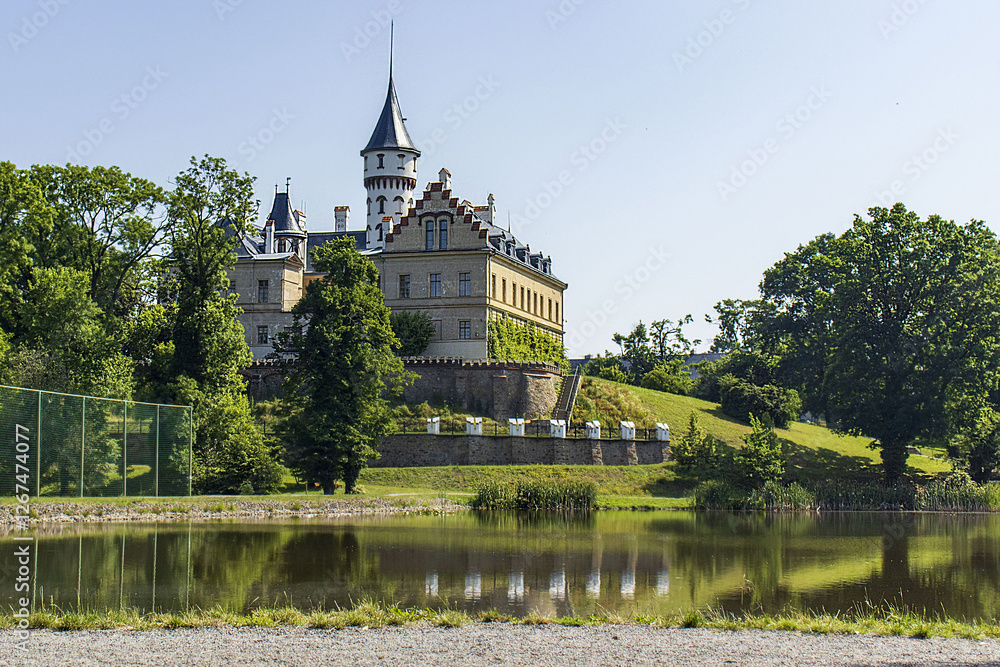 Castle building on a small grassy hill above the lake. The reflection of the castle on the water surface. Summer, sky, travel. Nature with castle building. Castle building on a small grassy hill above the lake. The reflection of the castle on the water surface. Summer, sky, travel. Nature with castle building.