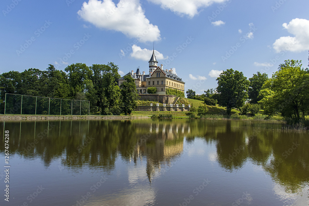 Castle building on a small grassy hill above the lake. The reflection of the castle on the water surface. Summer, sky, travel. Nature with castle building. Castle building on a small grassy hill above the lake. The reflection of the castle on the water surface. Summer, sky, travel. Nature with castle building.