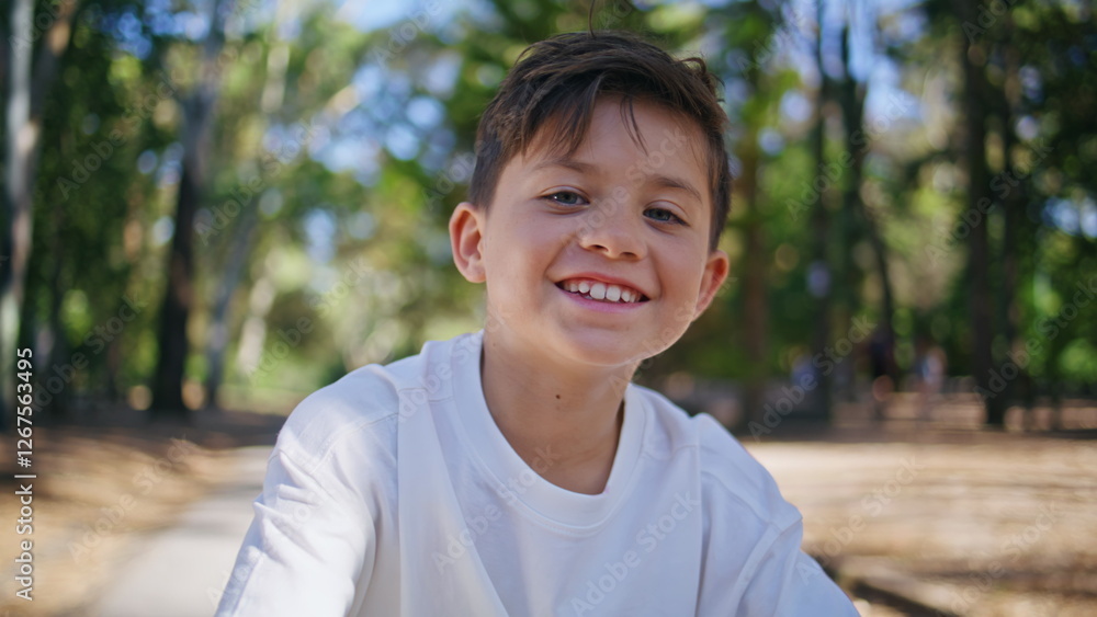 Cheerful kid looking camera at sunshine forest portrait. Happy child at park Cheerful kid looking camera at sunshine forest portrait. Happy child at park