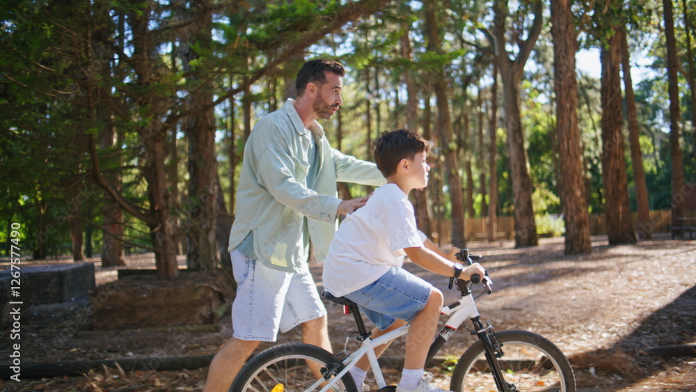 Small son learning cycling at sunny park. Boy driving cycle with father help Small son learning cycling at sunny park. Boy driving cycle with father help