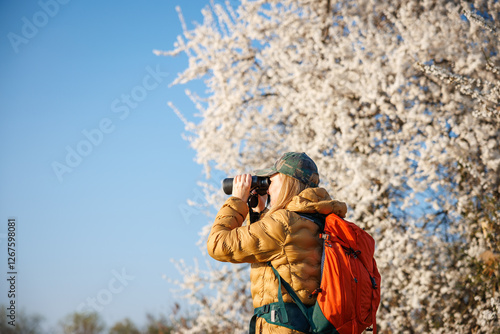 Bird watching. Woman ornithologist with binoculars observes birds arriving in spring in blooming nature