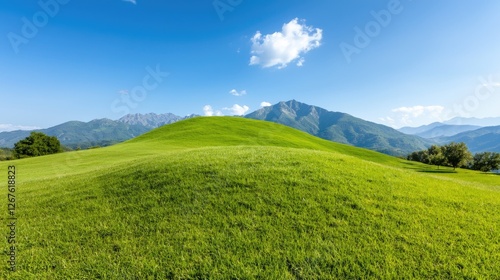 Vibrant green grassy hill rolling towards distant majestic mountains under a bright blue summer sky.