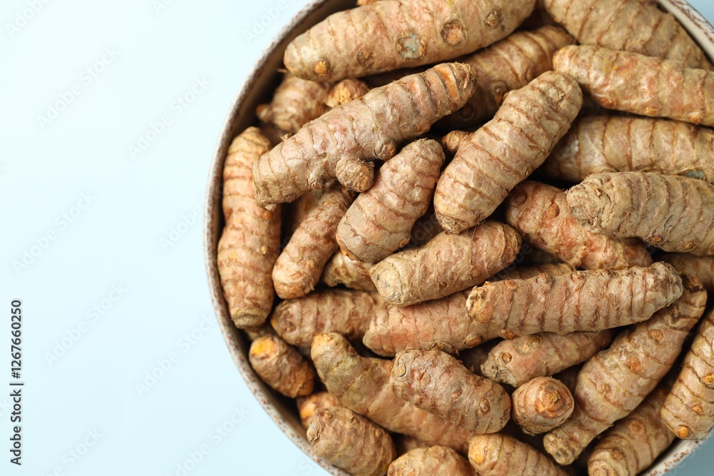 Tumeric rhizomes in bowl on light blue background, top view Tumeric rhizomes in bowl on light blue background, top view
