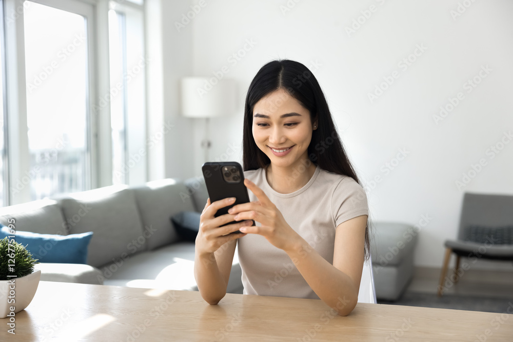 Pretty Asian woman sitting at table, holding her phone, reading message, browsing social media, looking through web page for information, taking moment for personal leisure alone at home. Fun, tech Pretty Asian woman sitting at table, holding her phone, reading message, browsing social media, looking through web page for information, taking moment for personal leisure alone at home. Fun, tech