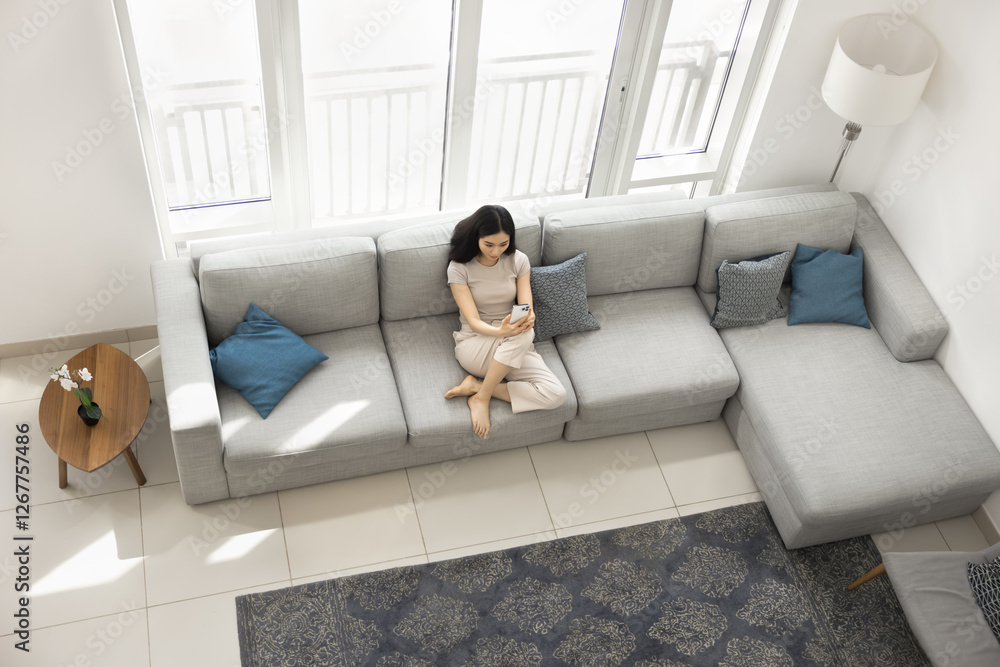 Woman sit on large sofa with smartphone, texting, browsing phone, watch videos, scrolling through social media, make videocall with friend, spend time, relaxing in quiet, comfortable space, above view Woman sit on large sofa with smartphone, texting, browsing phone, watch videos, scrolling through social media, make videocall with friend, spend time, relaxing in quiet, comfortable space, above view
