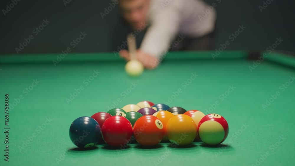 Blurred player in light shirt and dark trousers leans over green pool table, gripping cue stick with deep concentration. Eyes locked on balls, posture steady, creating tension in dimly lit game room
