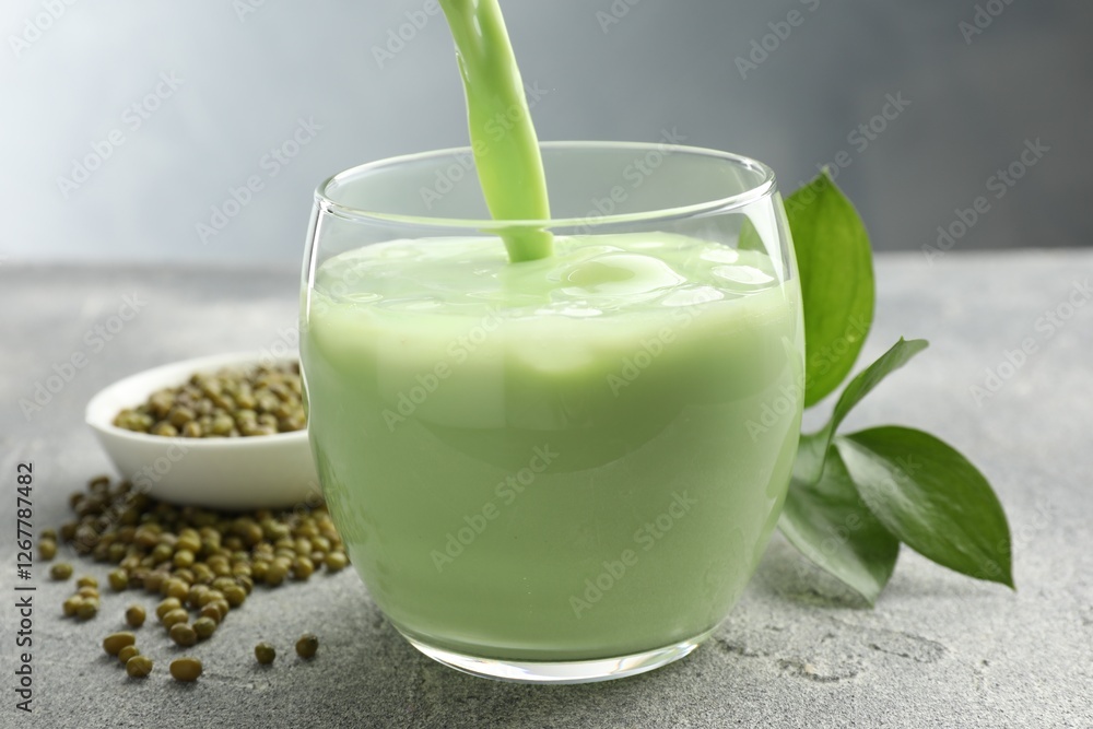 Pouring fresh mung bean juice in glass at grey table, closeup Pouring fresh mung bean juice in glass at grey table, closeup