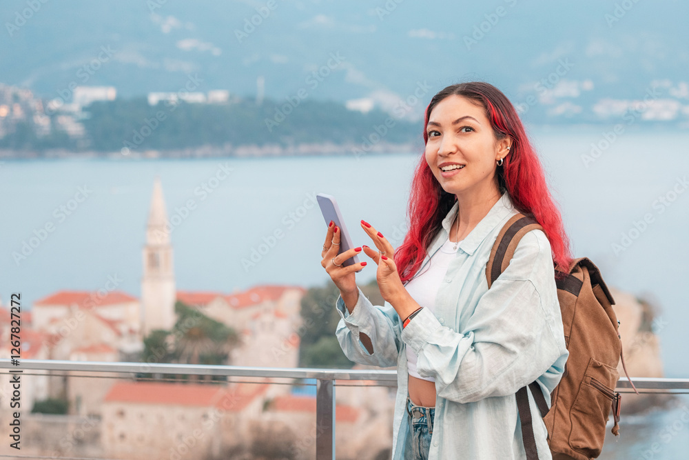 A female tourist with a backpack and phone stands against the backdrop of Budva, Montenegro, highlighting the concept of travel connection SIM cards, roaming rates, and internet costs.