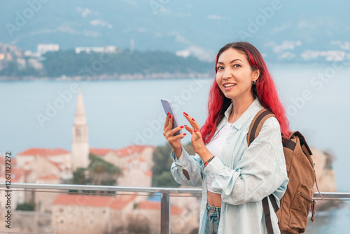 Obraz na płótnie A female tourist with a backpack and phone stands against the backdrop of Budva, Montenegro, highlighting the concept of travel connection SIM cards, roaming rates, and internet costs. w salonie
