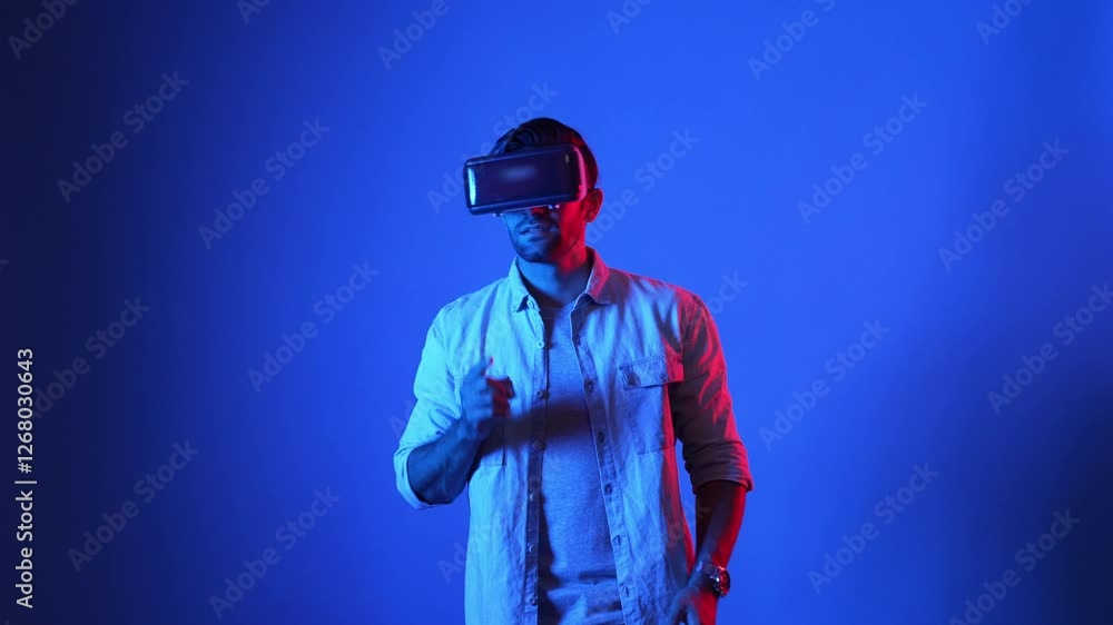 Professional gamer wearing VR headset while playing shooting game at metaworld. Male model making holding gun movement while standing at blue background by using virtual reality goggles. Apparatus. Professional gamer wearing VR headset while playing shooting game at metaworld. Male model making holding gun movement while standing at blue background by using virtual reality goggles. Apparatus.