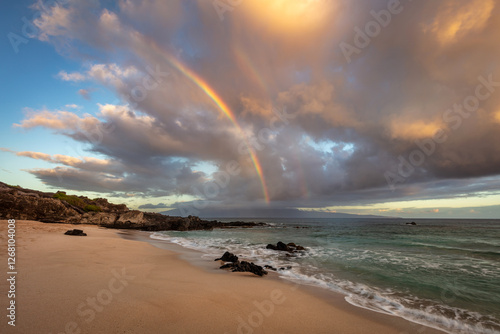 A dreamy rainbow on the beach with a dramatic sky at Oneloa Beach, Maui