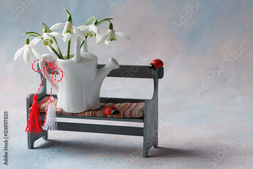 Card for the holiday of March 1, Martisor, Baba Marta. Decorative bench with a watering can, a bouquet of snowdrops, red and white symbol of Martenitsa, copy space