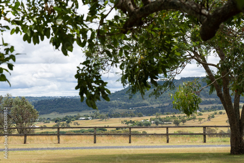 Scenic Australian countryside framed by lush green tree branches, overlooking rolling hills and farms. A tranquil rural landscape bathed in natural light.
