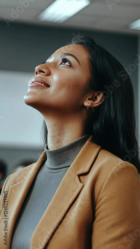 Woman in a brown blazer looks up thoughtfully during a seminar in a modern conference room
