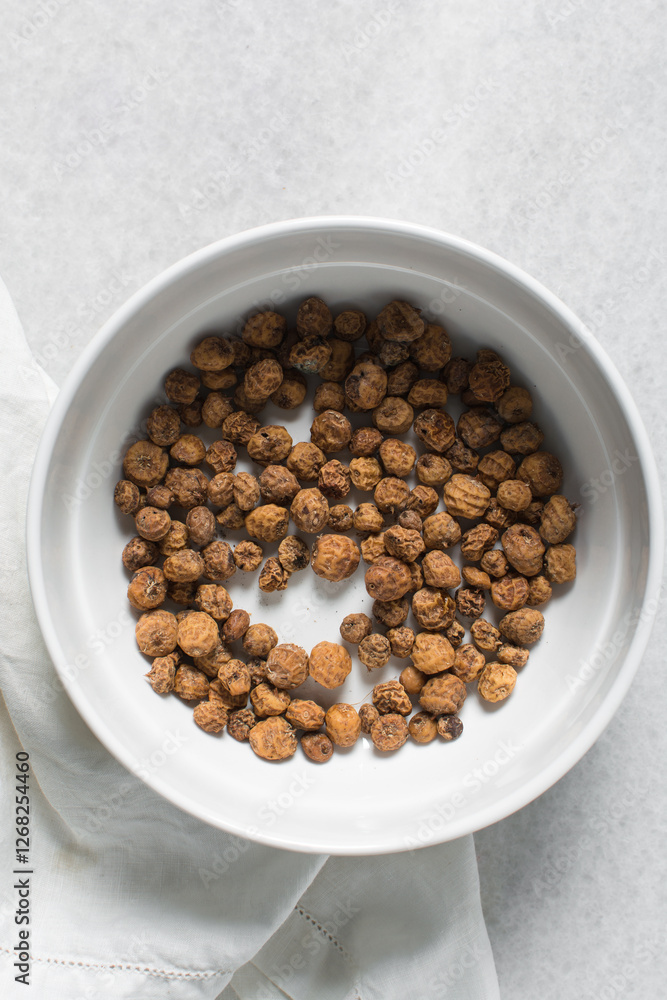 Overhead view of dried tiger nuts in a white bowl. top view of Yellow Nutsedge in a bowl Overhead view of dried tiger nuts in a white bowl. top view of Yellow Nutsedge in a bowl