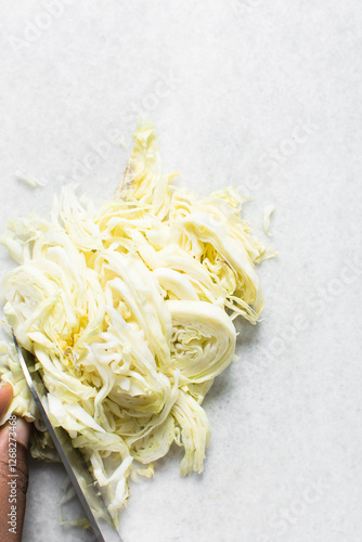 Overhead view of cabbage being sliced on a marble countertop, top view of cabbage leaves being shredded, green cabbage being sliced