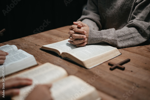 фотографія Group of Christians sit together and pray around a wooden table with blurred open Bible pages in their homeroom