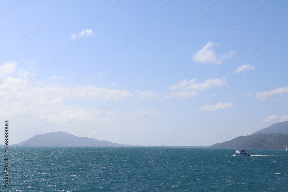 Lush marine scenery featuring a bright blue ocean and distant hills on a sunny day. A small boat navigates the tranquil waters, enhancing the serene outlook of the coastline Lush marine scenery featuring a bright blue ocean and distant hills on a sunny day. A small boat navigates the tranquil waters, enhancing the serene outlook of the coastline