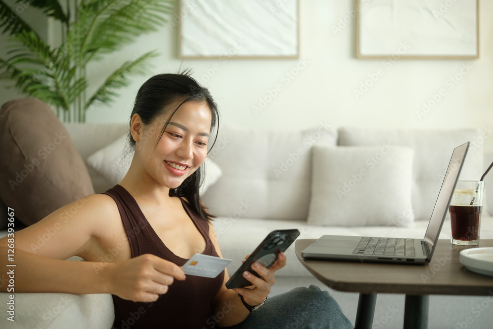 Satisfied young woman using her smartphone and credit card for online shopping while sitting in a modern living room. Satisfied young woman using her smartphone and credit card for online shopping while sitting in a modern living room.