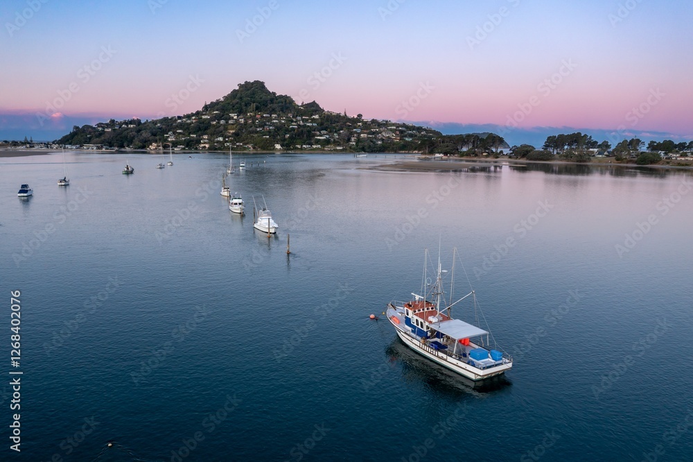 Fototapeta premium Tranquil morning scene on the water. Fishing boat navigates calm waters near coastal town. Peaceful harbor at dawn. Tairua, Coromandel Peninsula, New Zealand