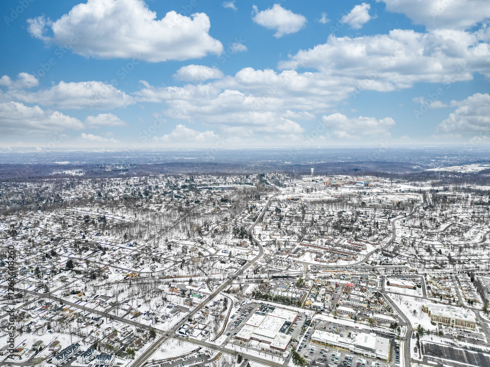Naklejka premium Aerial drone view of New Providence, New Jersey, covered in snow. The frozen landscape highlights roads, homes, and infrastructure, showcasing the suburban town in the cold season.