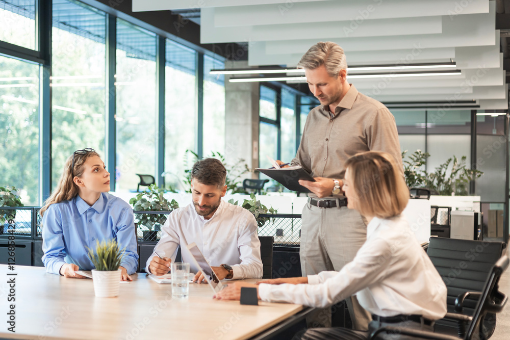 Handsome man gesturing and discussing something while his coworkers listening to him sitting at the office table. Handsome man gesturing and discussing something while his coworkers listening to him sitting at the office table.