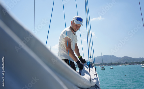Male captain on deck of sailboat unpacking sails pulling zipper