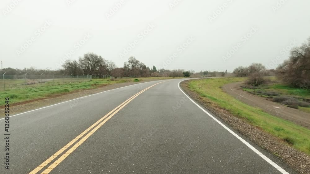 Paved road passing through green fields with autumn vegetation during a cloudy daytime Paved road passing through green fields with autumn vegetation during a cloudy daytime
